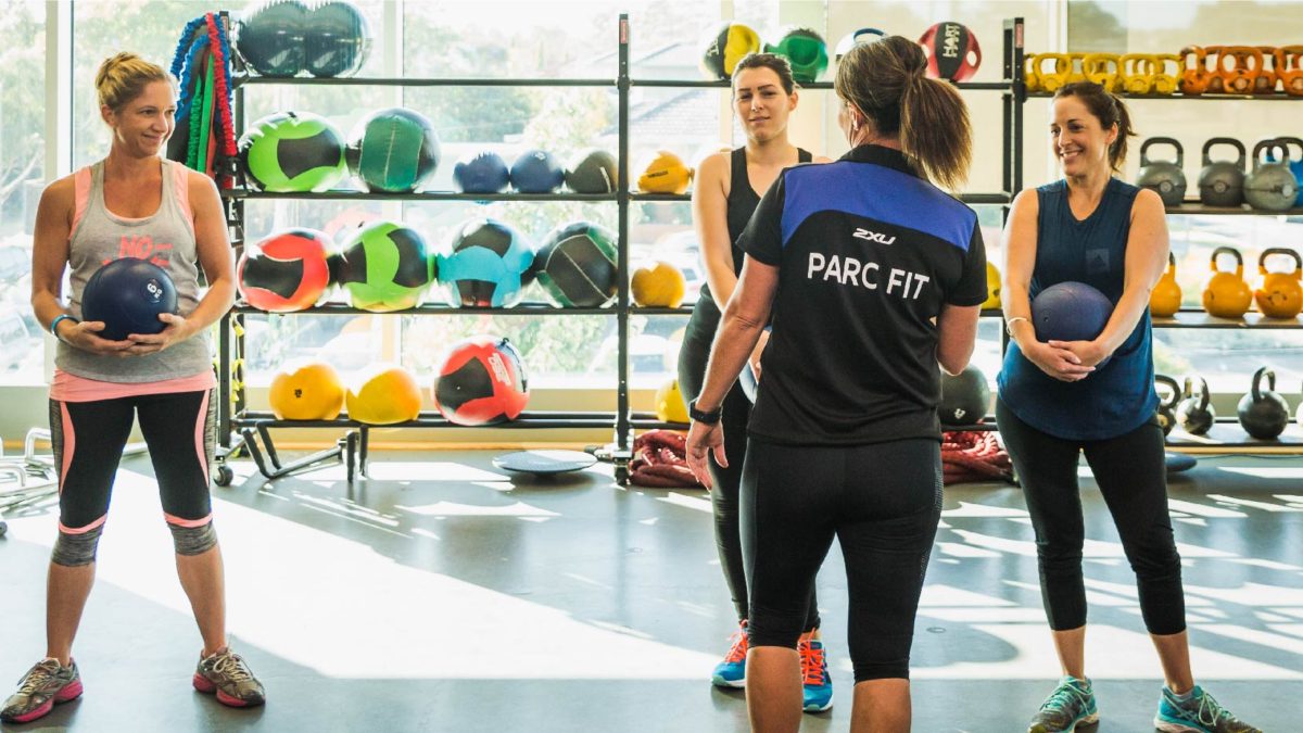 Ladies working out in a gym with a personal trainer.