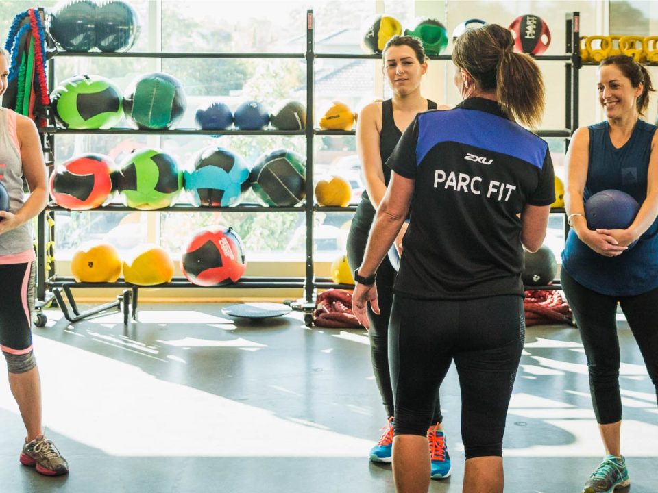 Ladies working out in a gym with a personal trainer.